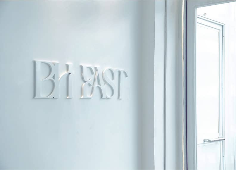 White wall with raised letters "BH EAST" next to an open door frame.