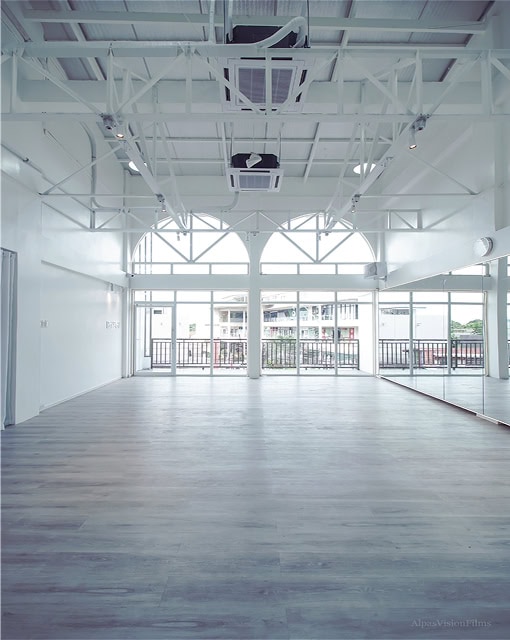 Bright, empty studio with white walls, large windows, and light wood flooring. High ceiling with exposed beams.
